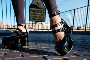 Close-up of kinky glamor fetish shoes on cobbled floor with danger signal behind.