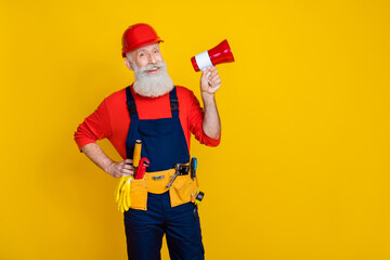 Photo of funky excited age man wear overall uniform red hard hat talking loud speaker empty space isolated yellow color background