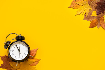 Daylight saving day. Fall Back. Black Alarm clock and autumn leaves on yellow background. Daylight...