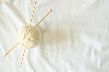 White wool thread ball with wooden bamboo knitting needles on white linen fabric background. Top...