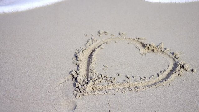 Sea waves covering heart drawn on beach sand. Symbol of romantic love on the beach. Concept of love, passion, relationships.