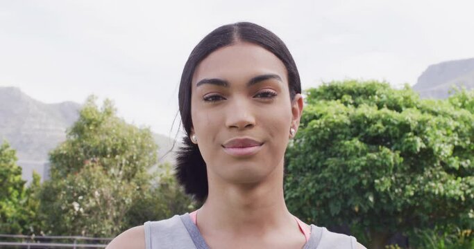 Video portrait of happy biracial non binary transgender woman smiling to camera outdoors