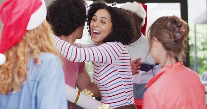 Happy biracial woman greeting diverse friends in santa hats with christmas presents at her home