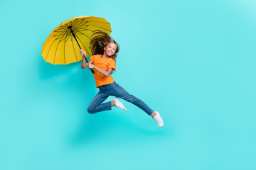 Full body size photo of chill pretty schoolgirl jumping air trampoline hold parasol excited positive mood empty space fall season isolated on cyan color background © deagreez