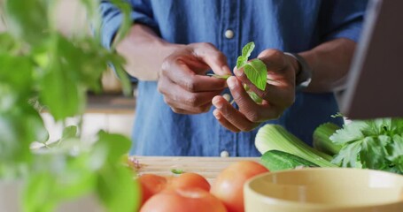 Midsection of african american man standing in kitchen and cooking dinner
