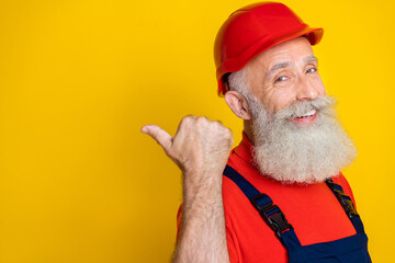 Photo of good mood funny senior guy dressed uniform overall red hardhat pointing thumb back empty...