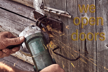 A man cuts the lock on an old wooden door with an angle grinder. Concept - we open doors.