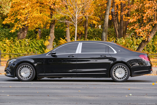 Sankt-Peterburg, RUSSIA - 12 october 2022 : Mercedes-Maybach S-class Sedan black rides on the road next to the autumn park. Young man driving a business car.
