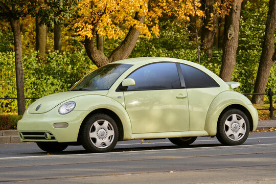 Sankt-Peterburg, RUSSIA - 12 october 2022 : An adult man drives a light green Volkswagen Beetle along the road near the autumn park. Beautiful budget car on the background of autumn foliage.
