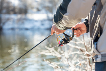 Fishing on the river in winter, the fisherman holds a fishing rod in his hands and spins the reel