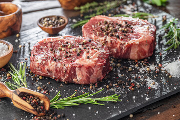 Raw Ribeye steaks with salt and herbs on grey board. Top view.