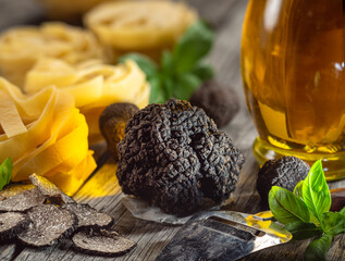 Black edible winter truffle, tagliatelle and fresh basil on wooden table. The most popular cooking...