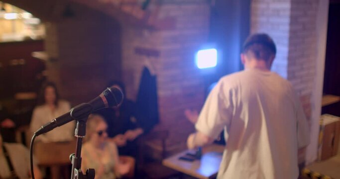 Stand-up comedian finish their monologue performance on stage. He puts the microphone on the rack, walks away happy. The priests in the bokeh clap, farewell. End of improvisation.