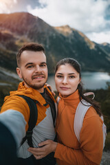 The young couple smiles and looks at the camera with a beautiful mountain and lake background....