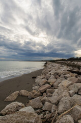 Fototapeta na wymiar I murazzi, tipici sbarramenti di pietre, sulla spiaggia del Lido di Venezia in una giornata invernale con il cielo pieno di nuvole grigie