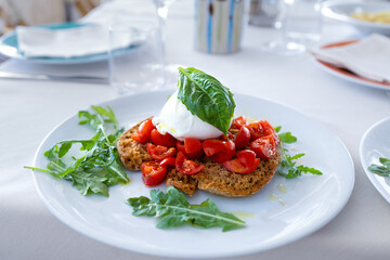 Typical Italian dish served on the plate: mozarella, cherry tomatoes, bread and arugula topped with...