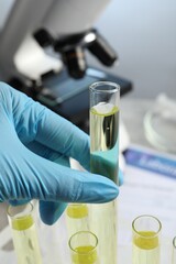 Doctor taking test tube with urine sample for analysis at table, closeup