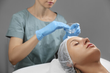 Fototapeta na wymiar Cosmetologist applying chemical peel product on client's face in salon