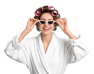 Beautiful young woman in bathrobe with hair curlers and sunglasses on white background