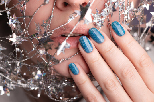 Beautiful woman with holiday manicure - blue glitter nails with silver twisted wire with stars. Closeup view. Nail care concept