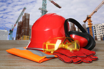 Safety equipment and tools on wooden surface and blurred view of construction site