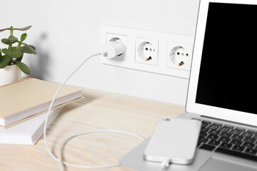 Laptop and smartphone charging on wooden table