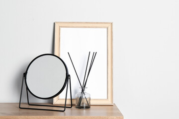 Fototapeta na wymiar Stylish mirror, reed diffuser and picture frame on table near light wall