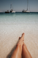 Kobiece nogi na plaży z widokiem na łodzie
