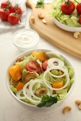 Bowl of delicious salad with Chinese cabbage, tomatoes and onion on white wooden table
