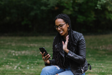 Black and Asian woman waving at phone on video chat in park 