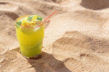 Glass of refreshing drink on sand. Space for text