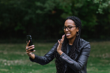 Black and Asian woman waving at phone on video chat in park