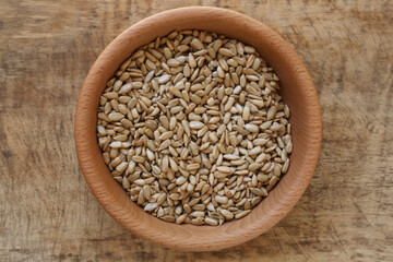 Bowl with organic sunflower seeds on wooden table, top view