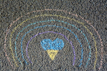 Rainbow with heart drawn by blue and yellow chalk on asphalt, top view