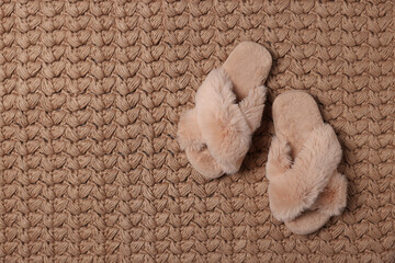 Fototapeta na wymiar Fluffy beige slippers on soft carpet, top view. Space for text