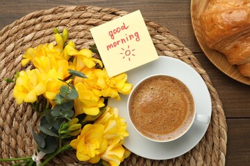 Cup of aromatic coffee with croissant, beautiful yellow freesias and Good Morning note on wooden...