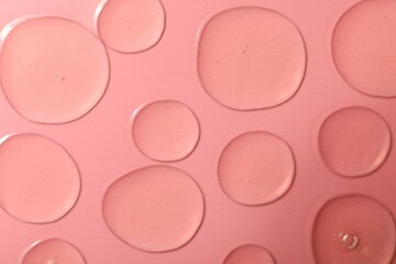 Drops of hydrophilic oil on pink background, flat lay