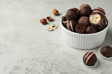 Different delicious chocolate truffles in bowl on light grey table. Space for text