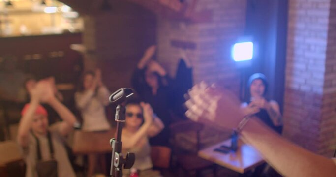 beginning stand-up comedian performance. He comes on stage, takes microphone with hand, the start live. Priests in bokeh clap, support the artist. He motivates activity with a hand gesture.