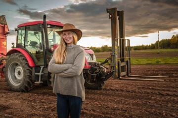 Shot of female farmer posing with crossed arms near combine harvester on field.