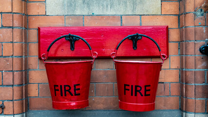 Two red fire buckets hanging from hooks on a brick wall