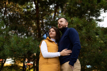 happy adult husband and wife in the autumn forest stand embracing and look into the distance