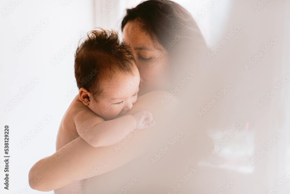 Wall mural intimate portrait of hispanic mother holding newborn baby daughter in her arms showing love and care