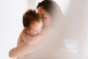 intimate portrait of hispanic mother holding newborn baby daughter in her arms showing love and care, with soft natural light. concept of bonding and motherhood