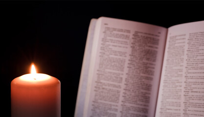 Fototapeta na wymiar burning wax candle illuminates book in the background
