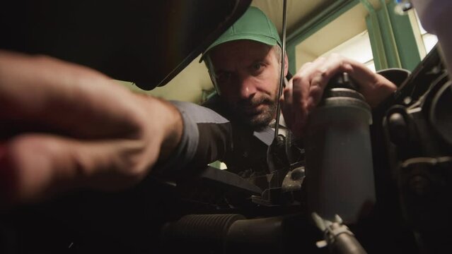 Low angle slowmo of middle aged Caucasian auto mechanic working under car bonnet in garage