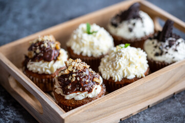 Cupcakes and muffins placed in wooden box. Chocolate and creme with nuts. Fresh home make baked sweets.