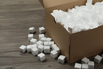 Cardboard box and styrofoam cubes on wooden floor, closeup