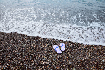 Fototapeta na wymiar Stylish lilac flip lops on pebble beach near sea. Space for text