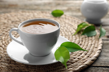 Green tea in white cup with leaves and wicker mat on table, closeup
